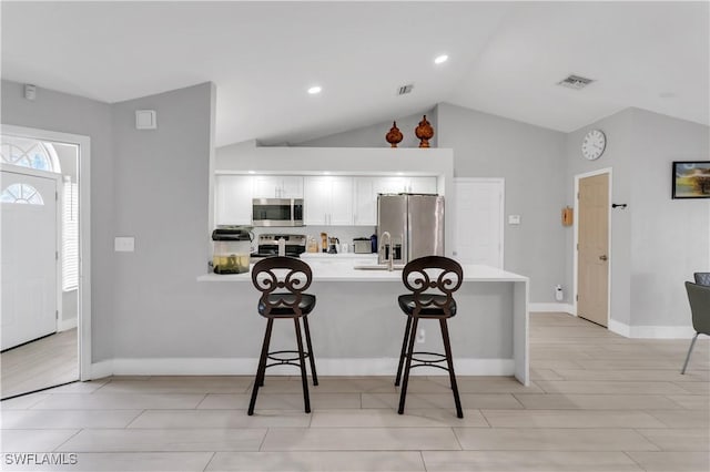 kitchen with a breakfast bar area, tasteful backsplash, vaulted ceiling, appliances with stainless steel finishes, and white cabinets