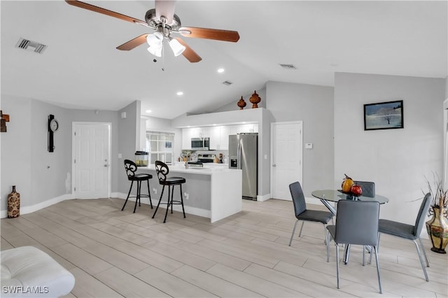 kitchen with vaulted ceiling, a breakfast bar area, white cabinets, kitchen peninsula, and stainless steel appliances