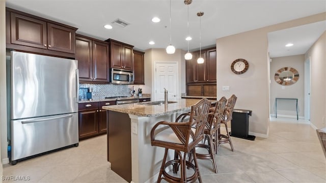 kitchen featuring sink, light stone counters, a center island with sink, appliances with stainless steel finishes, and pendant lighting