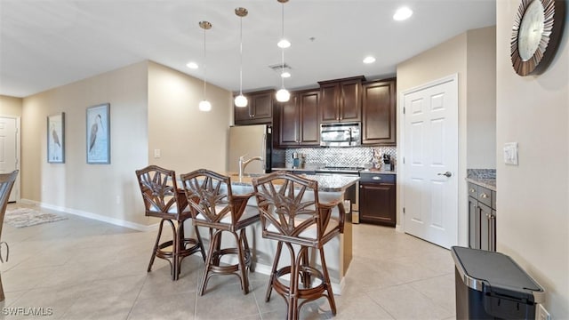 kitchen featuring an island with sink, decorative backsplash, hanging light fixtures, dark brown cabinetry, and stainless steel appliances