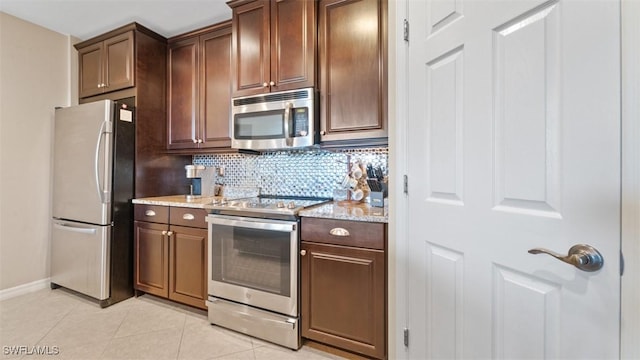 kitchen featuring light tile patterned floors, appliances with stainless steel finishes, tasteful backsplash, dark brown cabinetry, and light stone countertops