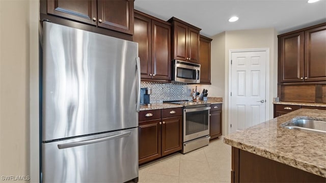 kitchen featuring appliances with stainless steel finishes, decorative backsplash, light tile patterned floors, light stone counters, and dark brown cabinetry