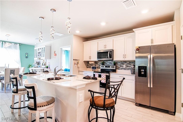 kitchen with stainless steel appliances, a center island with sink, pendant lighting, and white cabinets