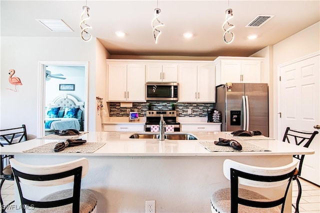 kitchen with sink, white cabinetry, stainless steel appliances, a kitchen breakfast bar, and an island with sink