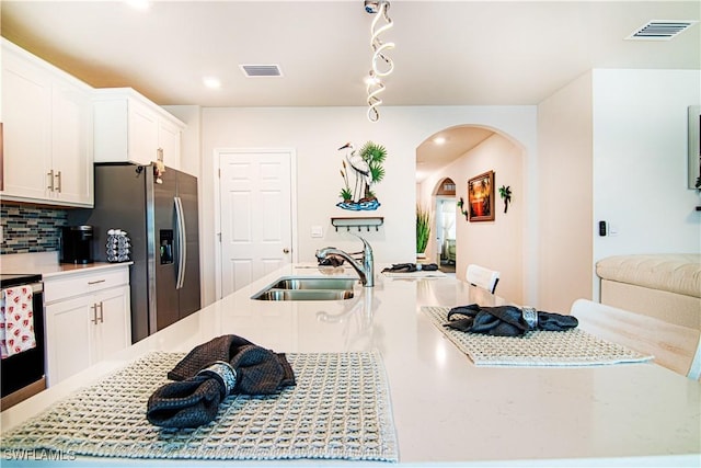 kitchen with sink, white cabinetry, stainless steel refrigerator with ice dispenser, tasteful backsplash, and an island with sink