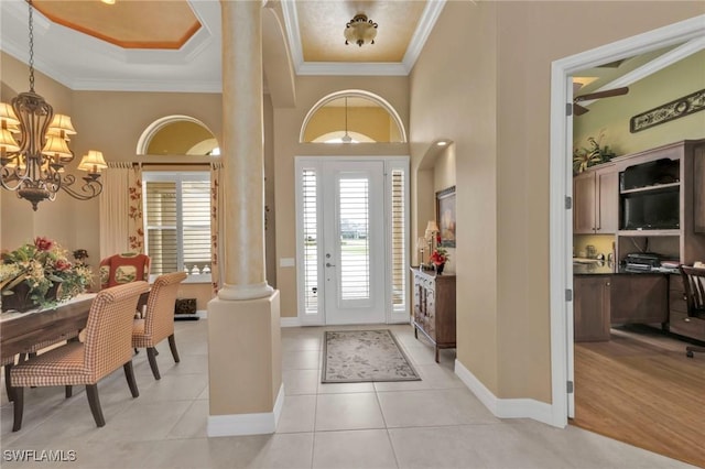 entryway with ornate columns, ornamental molding, light tile patterned floors, and an inviting chandelier