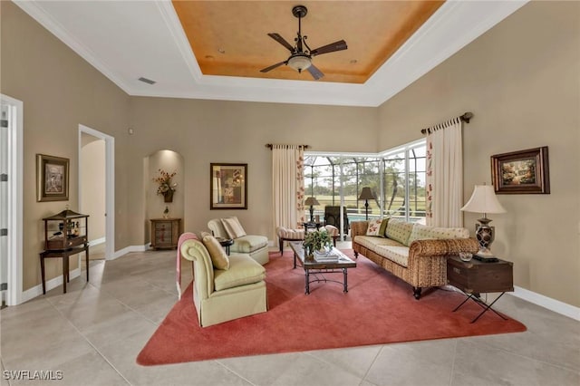 living room with light tile patterned floors, a tray ceiling, ornamental molding, and ceiling fan