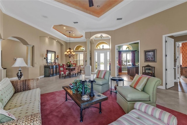 living room with a tray ceiling, ornamental molding, a chandelier, and ornate columns