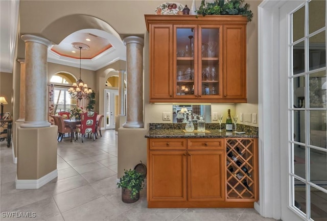 bar with decorative columns, a raised ceiling, and dark stone counters