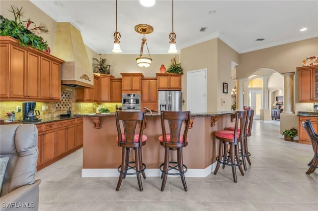 kitchen with pendant lighting, a breakfast bar area, premium range hood, dark stone countertops, and appliances with stainless steel finishes