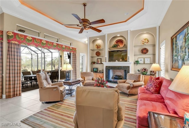 living room featuring built in shelves, a fireplace, ornamental molding, and a tray ceiling