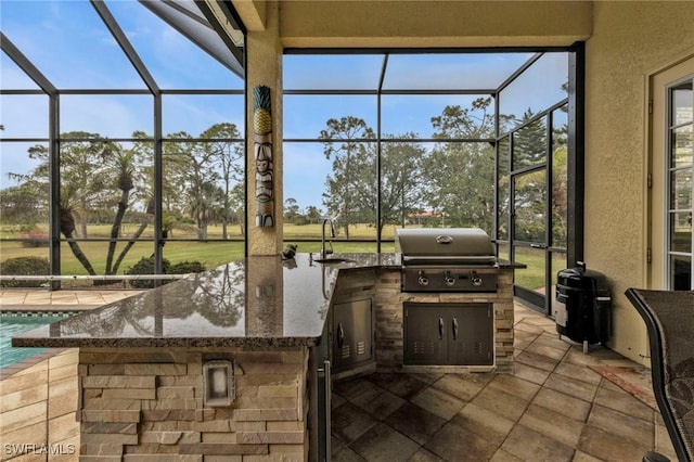 view of patio / terrace with a lanai, grilling area, a wet bar, and an outdoor kitchen