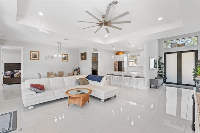 living room featuring a raised ceiling, ceiling fan, and french doors