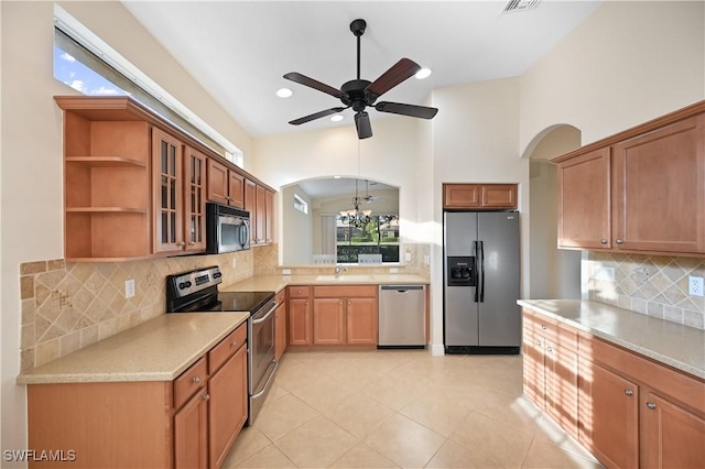 kitchen with light tile patterned flooring, sink, stainless steel appliances, ceiling fan with notable chandelier, and backsplash