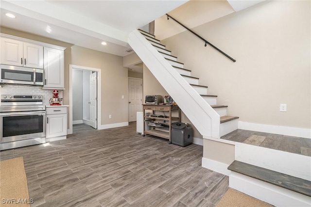 kitchen with wood-type flooring, appliances with stainless steel finishes, white cabinets, and decorative backsplash