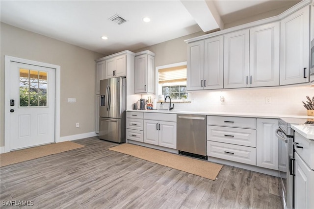 kitchen featuring beamed ceiling, backsplash, white cabinets, stainless steel appliances, and light wood-type flooring