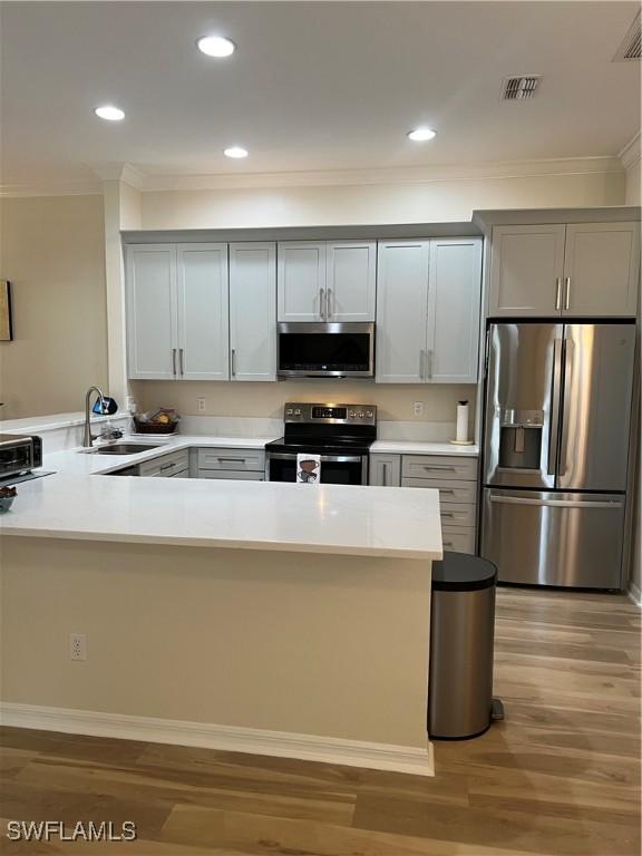 kitchen with a peninsula, stainless steel appliances, light countertops, light wood-style floors, and a sink