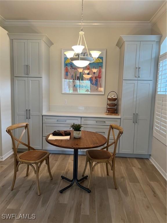 dining space with a notable chandelier, baseboards, light wood-style flooring, and crown molding