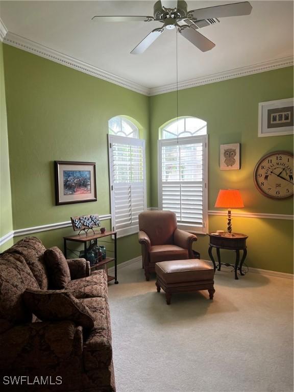 carpeted living area featuring a ceiling fan, baseboards, and crown molding