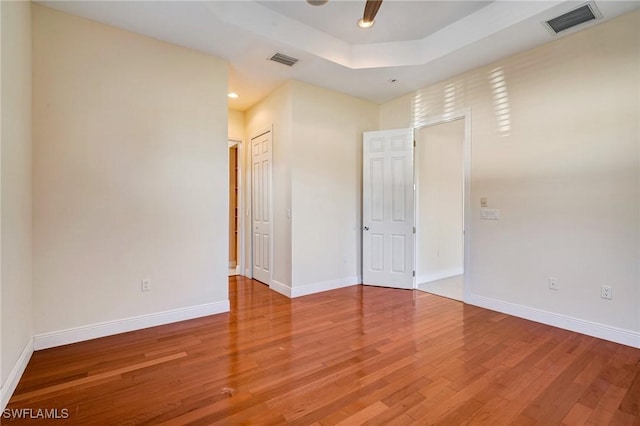 empty room with hardwood / wood-style flooring, ceiling fan, and a raised ceiling