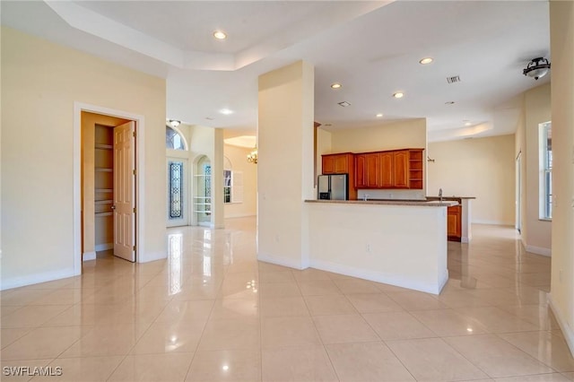 kitchen featuring sink, light tile patterned floors, kitchen peninsula, and stainless steel refrigerator with ice dispenser