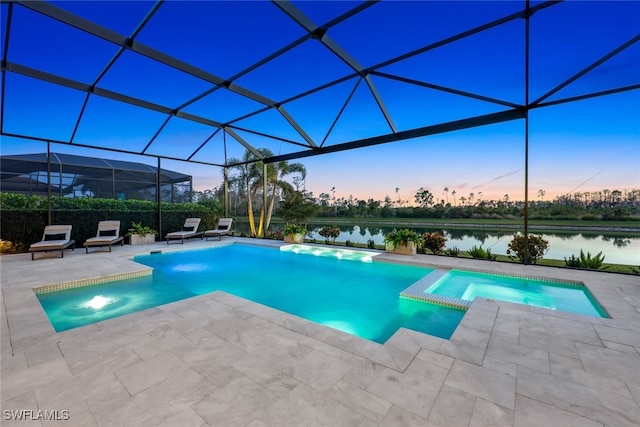 pool at dusk featuring pool water feature, a patio area, a water view, glass enclosure, and an in ground hot tub