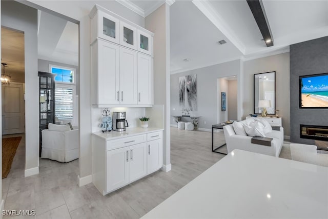 kitchen featuring crown molding, light hardwood / wood-style flooring, a large fireplace, white cabinets, and beamed ceiling