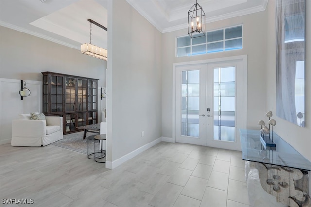 foyer featuring a raised ceiling, ornamental molding, an inviting chandelier, and french doors