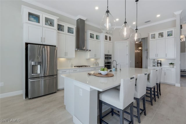 kitchen featuring appliances with stainless steel finishes, pendant lighting, white cabinetry, a kitchen island with sink, and wall chimney exhaust hood