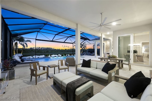 patio terrace at dusk featuring a water view, outdoor lounge area, ceiling fan, and a lanai