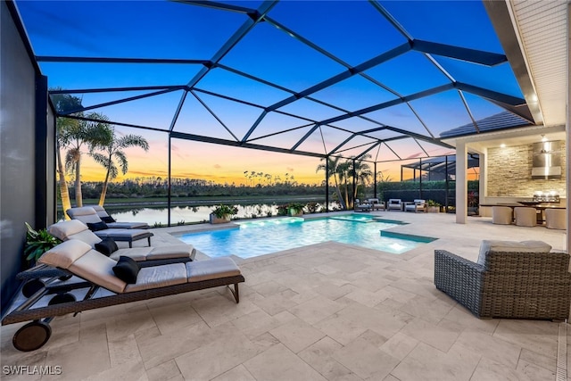 pool at dusk with a lanai, a patio, pool water feature, and a water view