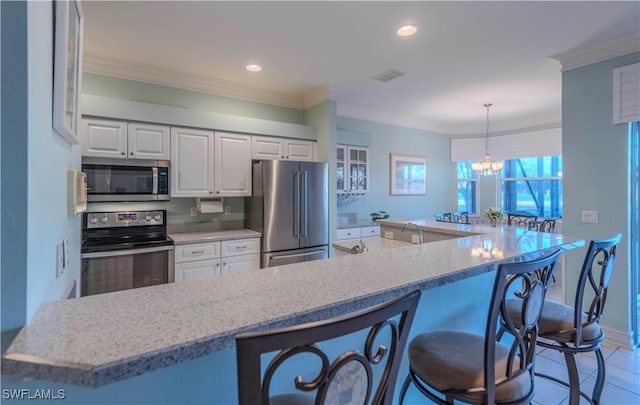 kitchen featuring appliances with stainless steel finishes, decorative light fixtures, white cabinetry, light stone counters, and crown molding