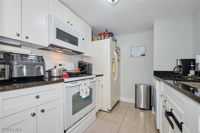 kitchen with light tile patterned floors, white appliances, white cabinetry, a textured ceiling, and dark stone counters