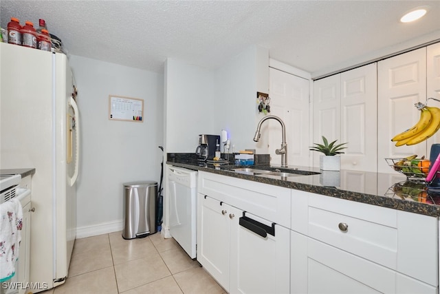 kitchen featuring sink, white cabinetry, light tile patterned floors, dishwasher, and dark stone counters