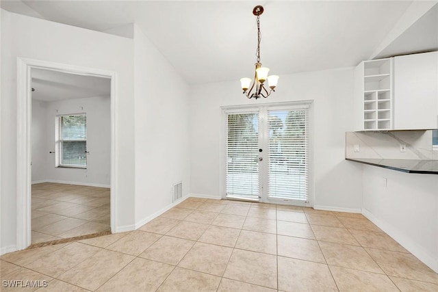 unfurnished dining area with plenty of natural light, light tile patterned floors, a chandelier, and french doors