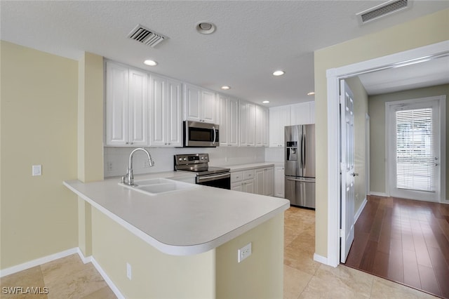 kitchen featuring sink, white cabinets, backsplash, kitchen peninsula, and stainless steel appliances