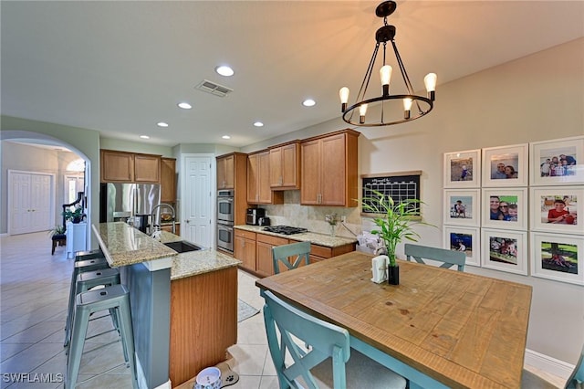 kitchen with an island with sink, sink, backsplash, hanging light fixtures, and stainless steel appliances