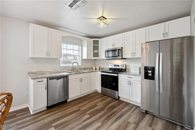 kitchen with appliances with stainless steel finishes, white cabinetry, sink, light stone counters, and dark wood-type flooring