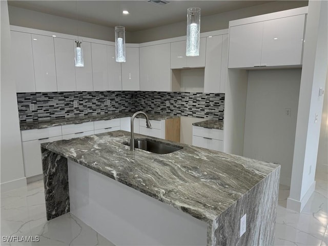 kitchen featuring a kitchen island with sink, sink, decorative light fixtures, and white cabinets