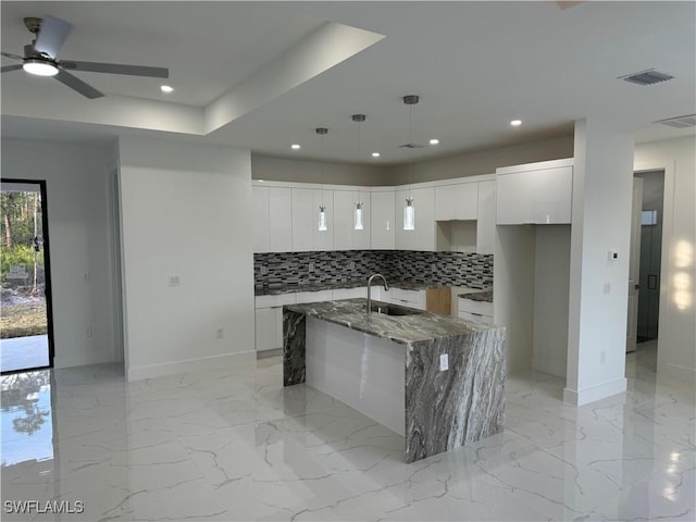 kitchen featuring stone counters, a kitchen island with sink, sink, and white cabinets