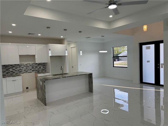 kitchen featuring sink, white cabinetry, hanging light fixtures, an island with sink, and backsplash