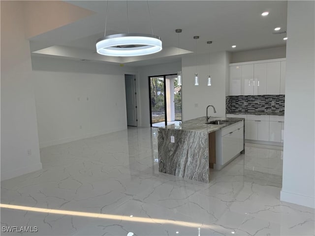 kitchen featuring pendant lighting, sink, backsplash, white cabinets, and light stone counters