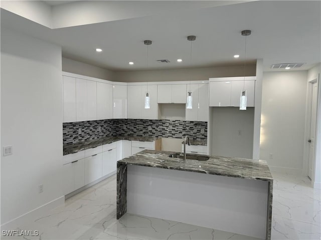 kitchen with sink, decorative light fixtures, an island with sink, and white cabinets