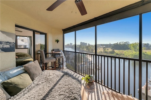 sunroom featuring ceiling fan and a water view