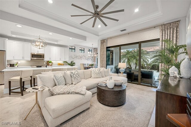 living room featuring ornamental molding, a tray ceiling, and ceiling fan with notable chandelier