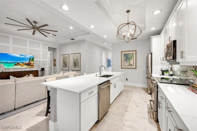 kitchen with a kitchen bar, sink, a tray ceiling, stainless steel appliances, and white cabinets