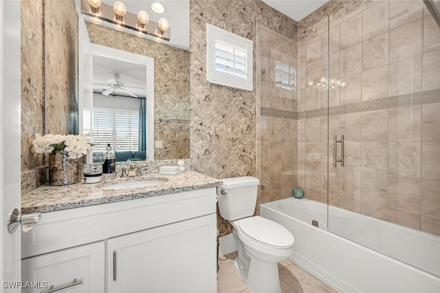 bathroom featuring tile patterned flooring, toilet, shower / bath combination with glass door, vanity, and a ceiling fan