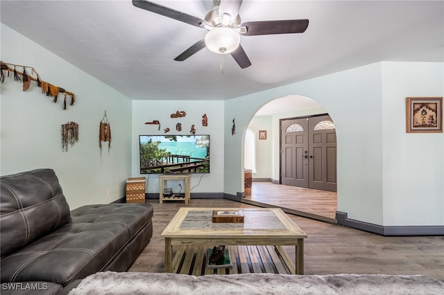 living room featuring a ceiling fan, baseboards, arched walkways, and wood finished floors