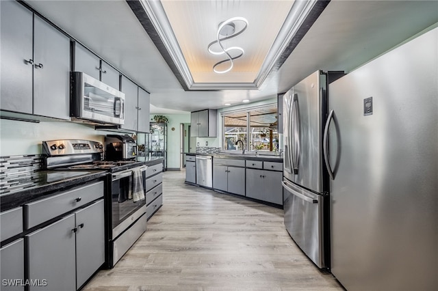 kitchen featuring sink, light hardwood / wood-style flooring, gray cabinets, stainless steel appliances, and a raised ceiling