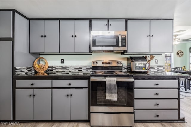 kitchen with gray cabinetry, stainless steel appliances, visible vents, light wood-style floors, and dark countertops